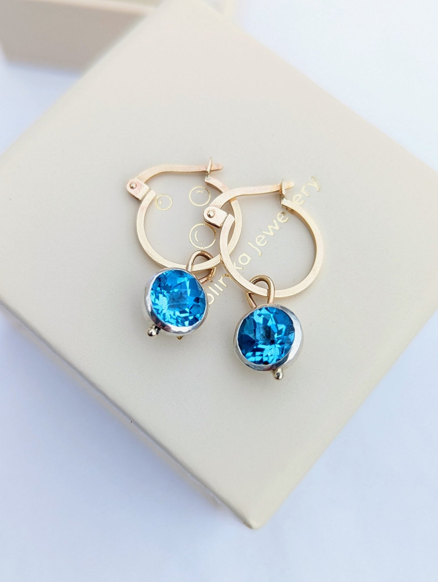 9ct gold hoop earrings with removable blue topaz charms on an ivory jewellery box handmade by Booblinka Jewellery