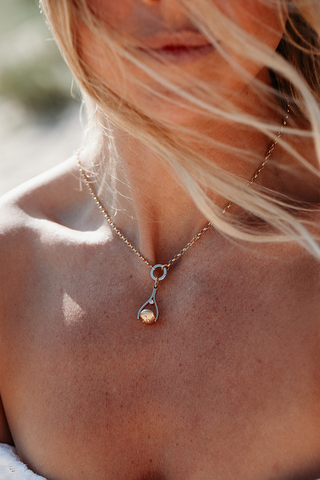 Close-up of a person wearing a gold necklace with a small spinning pendant made by Booblinka Jewellery.