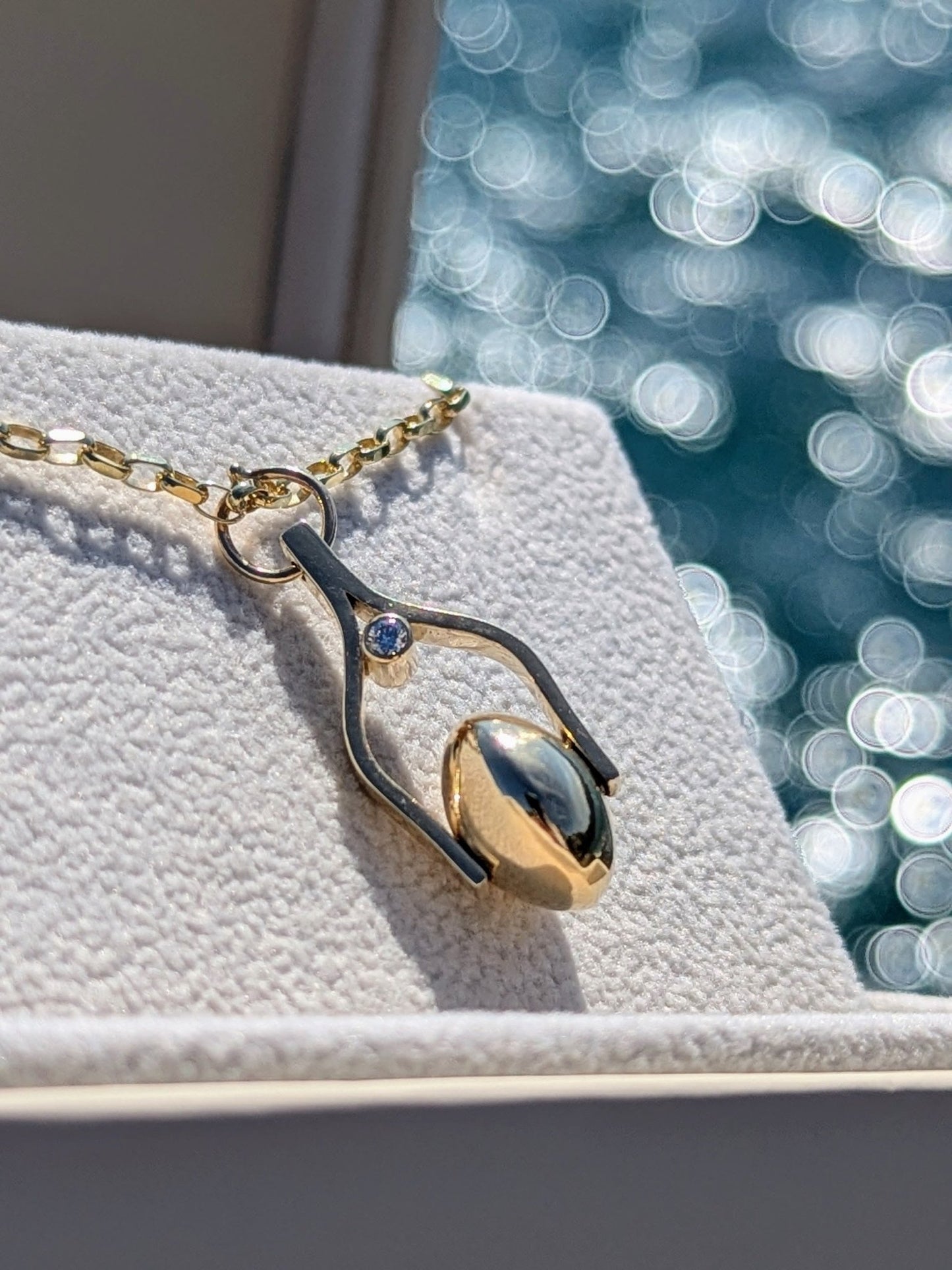 Gold Spinning Necklace with Ocean Diamonds in a plush jewellery box with shimmering ocean in background. Made by Booblinka Jewellery.
