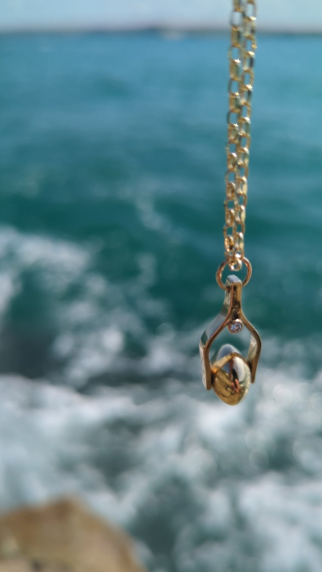 Video of gold spinning necklace with two ocean diamonds moving above the ocean. Made by Booblinka Jewellery.