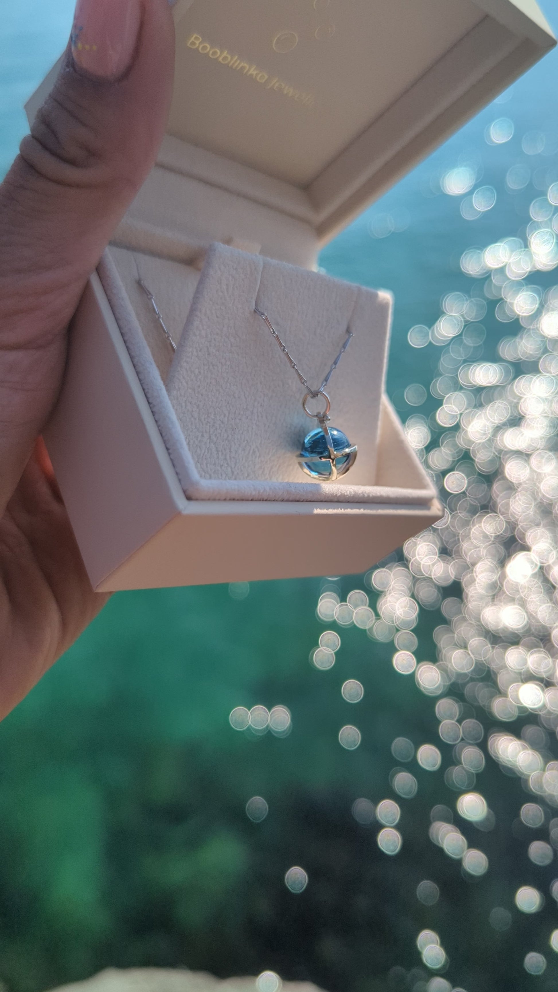 video of Fairtrade white gold necklace with Swiss Blue Topaz, shown hanging over a Booblinka Jewellery box with ocean tones.