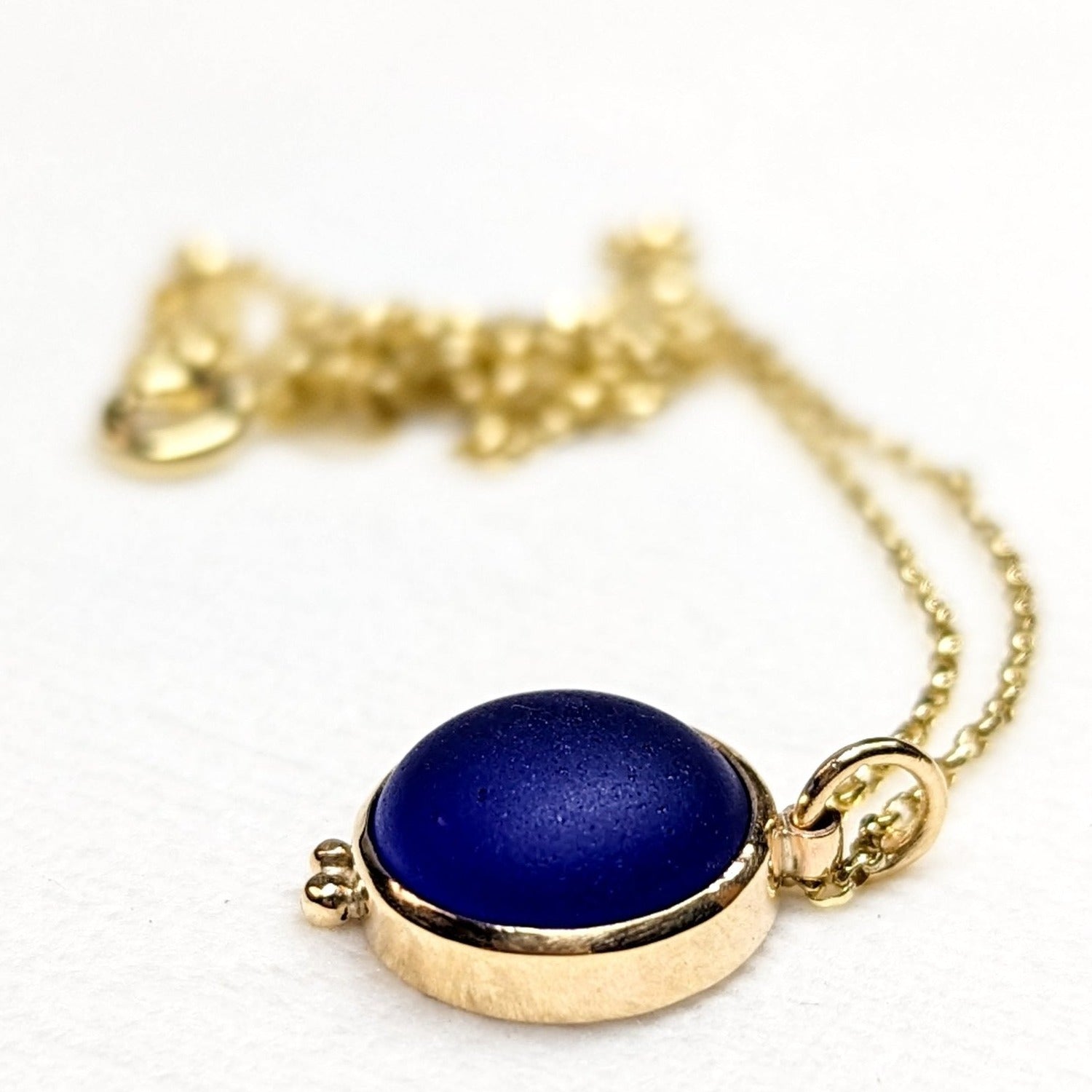 9ct Gold Cobalt Blue Sea Glass Necklace  Side angle view of a cobalt blue sea glass necklace in a solid 9 carat gold bezel setting with small gold granules, highlighting the pendant’s texture and depth by Booblinka Jewellery