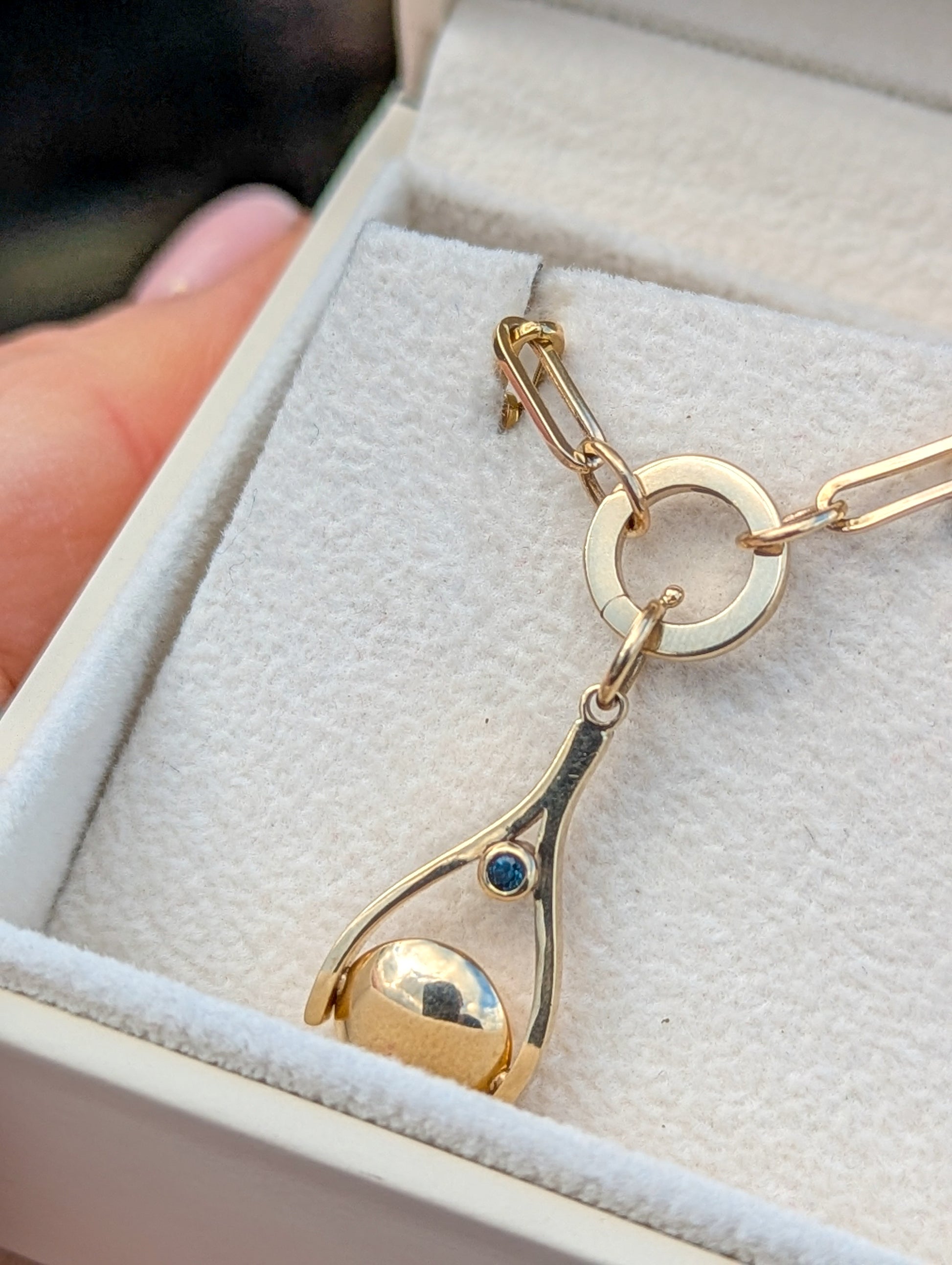 Gold spinning pendant with a teal sapphire  in a white jewellery box made by Booblinka Jewellery