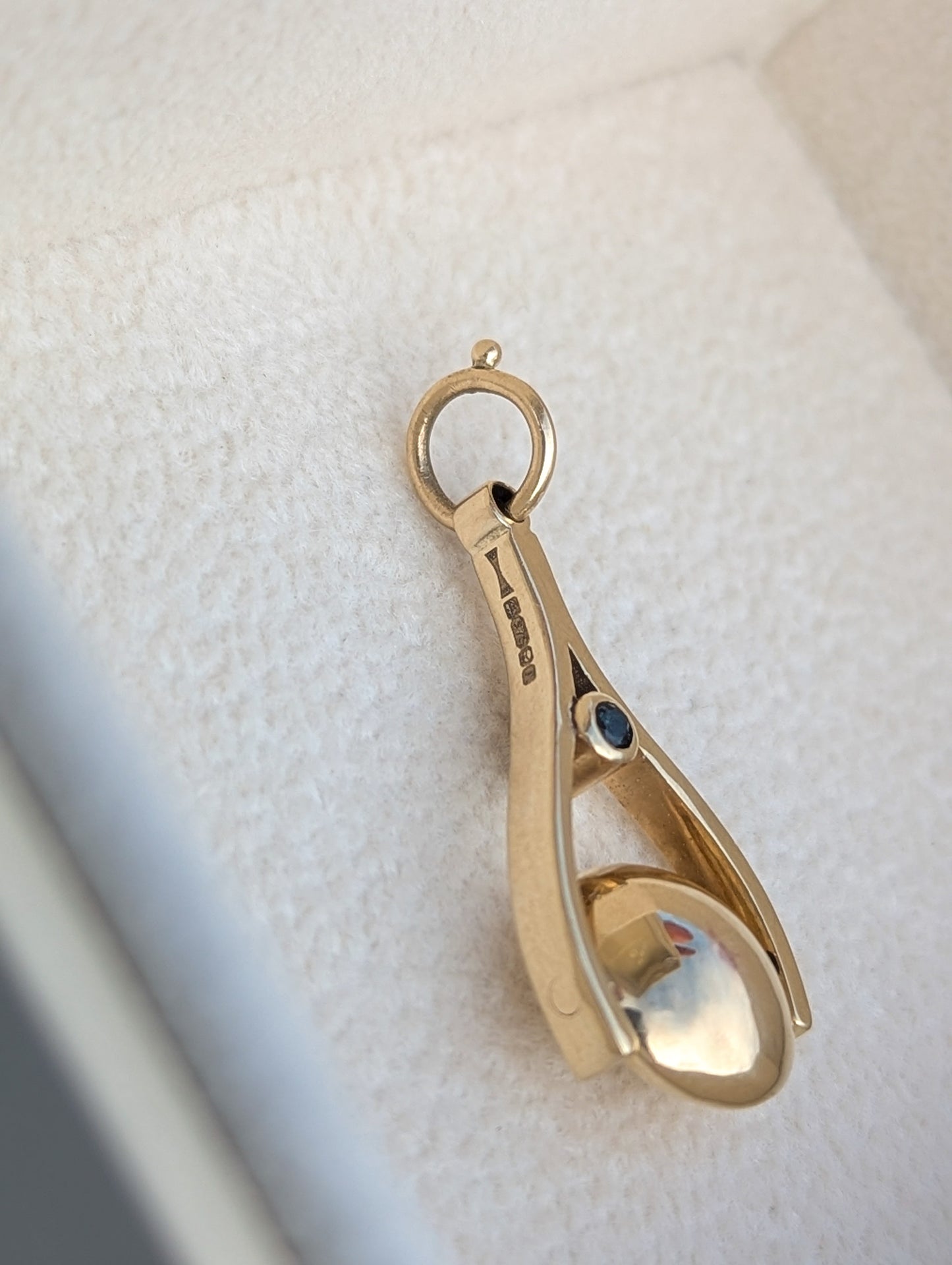 Detail of a hallmark on a 9c Gold spinning pendant with a teal sapphire on a white background made by Booblinka Jewellery.