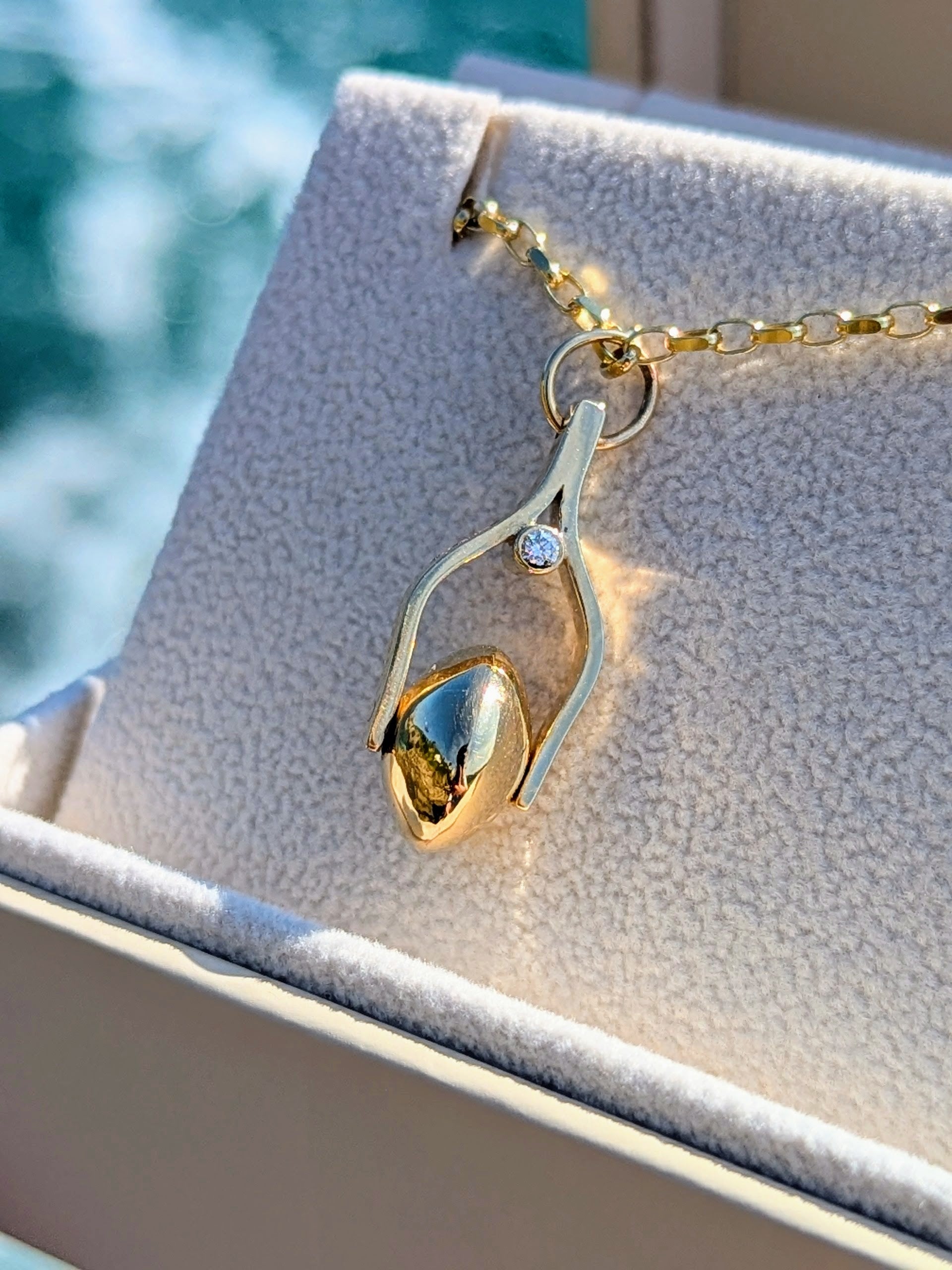 Gold necklace with a spinning pendant with ocean diamond on a textured surface with a blurred ocean background