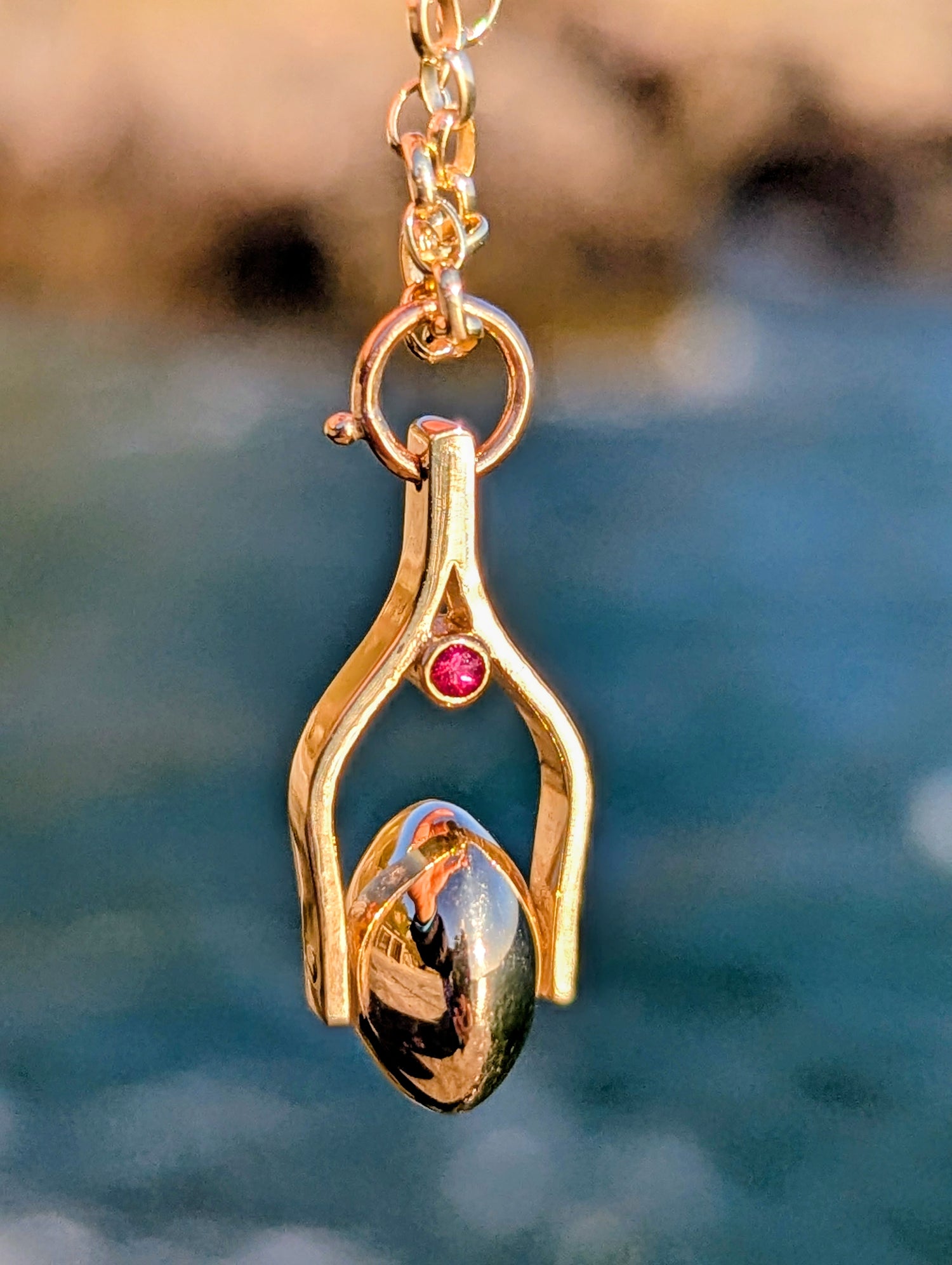 Gold necklace with a spinning pendant with a pink tourmaline gemstone against a blurred natural background