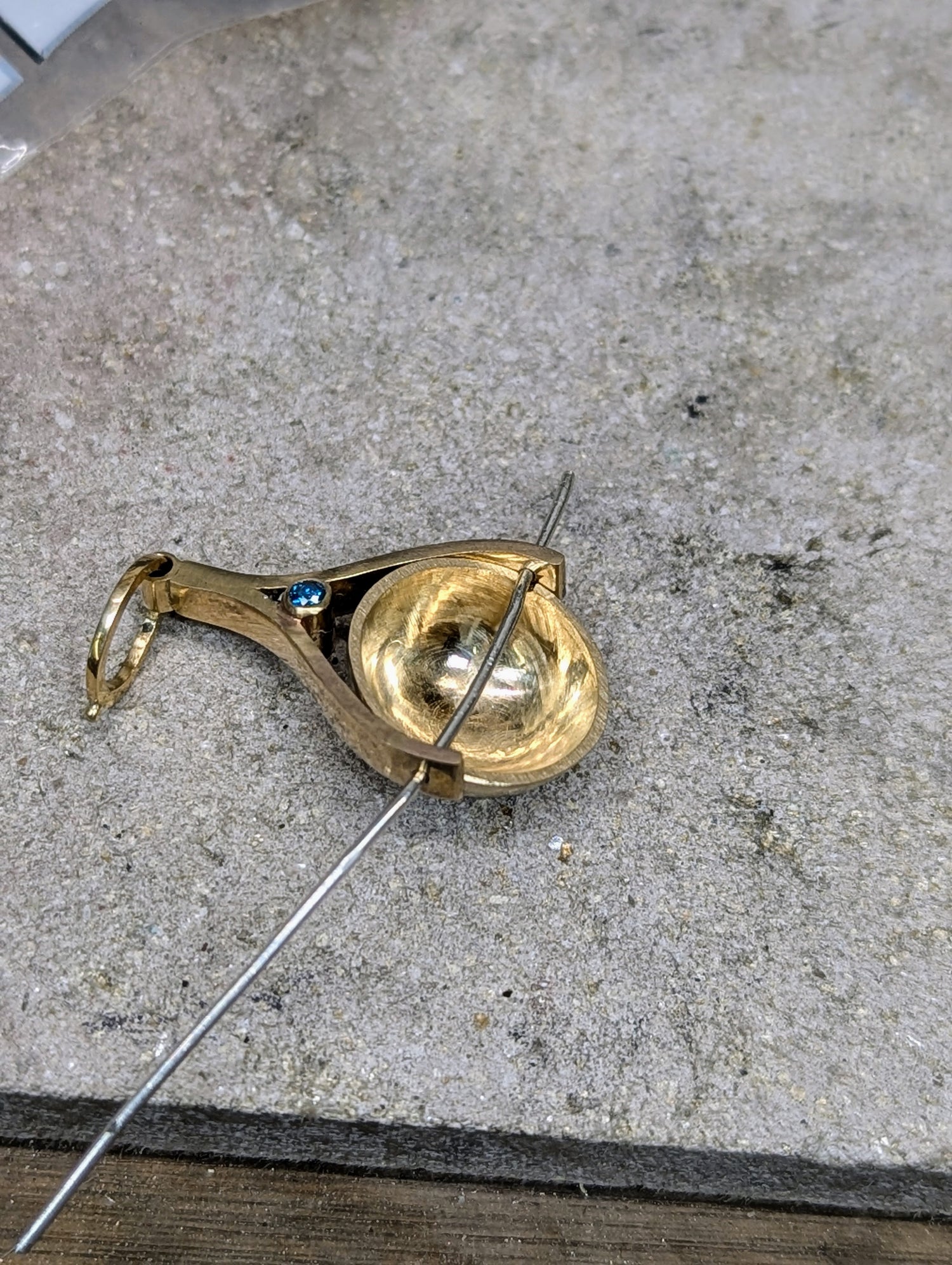 Gold spinning pendant in making with blue diamond on a concrete surface
