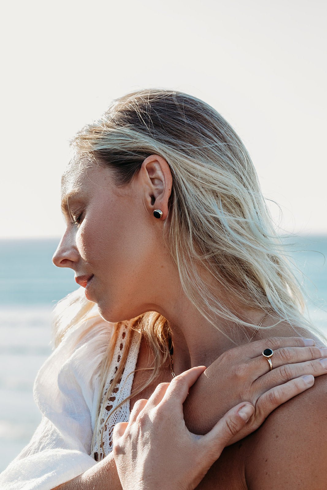 Woman wearing one of the opaque black sea glass stud earrings handmade in solid 9ct yellow gold, showing its size on the ear.