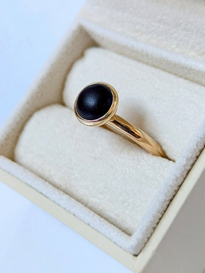 Black sea glass ring in a jewellery box showing the handmade 9ct yellow gold band and rounded setting