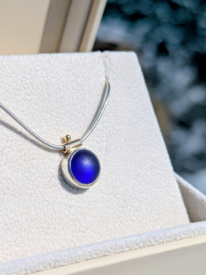 Blue round sea glass necklace with snake chain and gold detail in an open ivory jewellery box glowing in a sunshine
