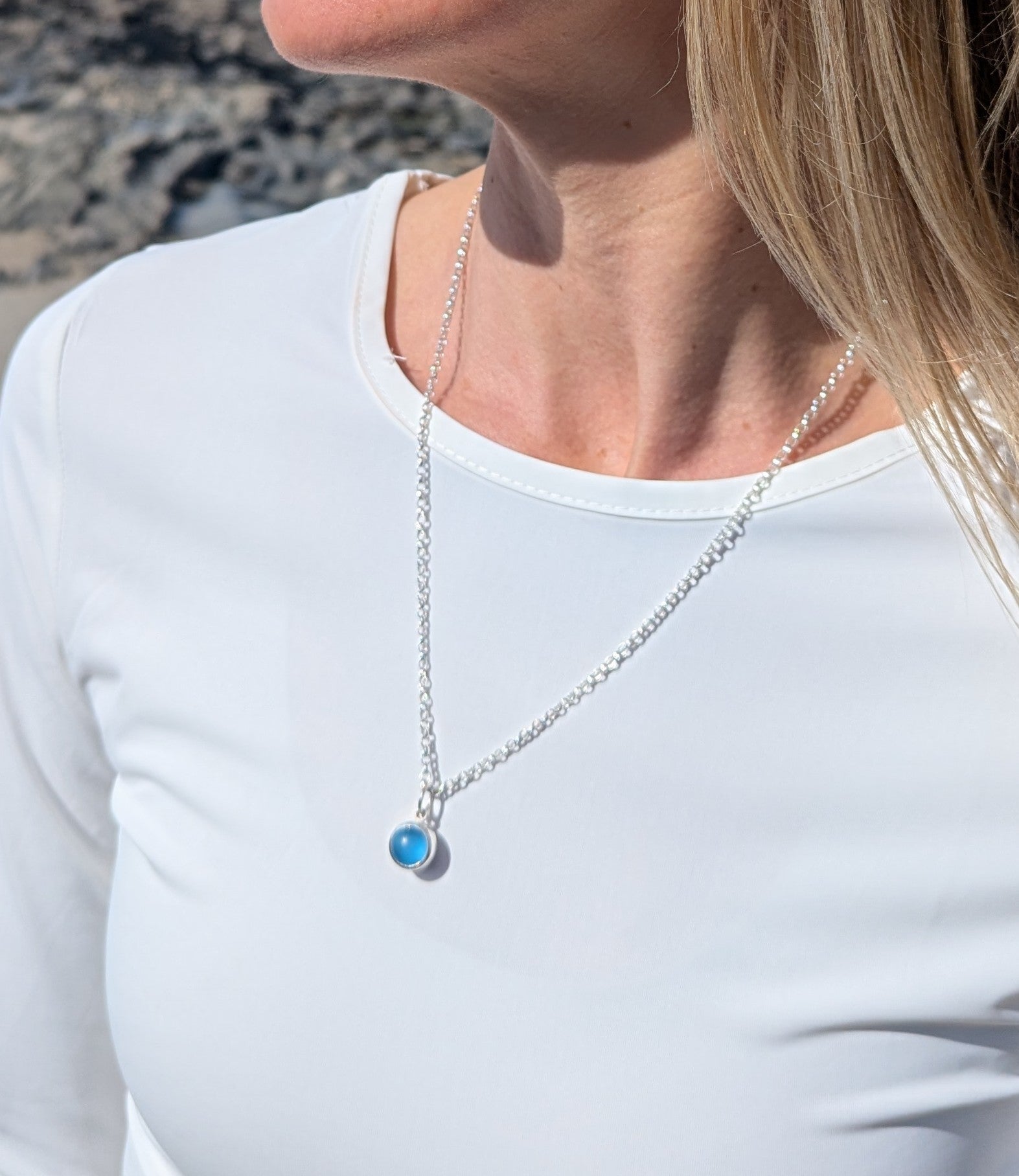Detail of the blue round silver necklace on woman's neck on white top