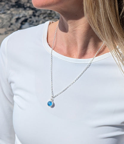 Detail of the blue round silver necklace on woman's neck on white top