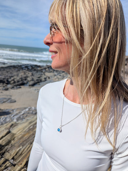 Woman wearing the blue round sea glass silver necklace on white top with beach background