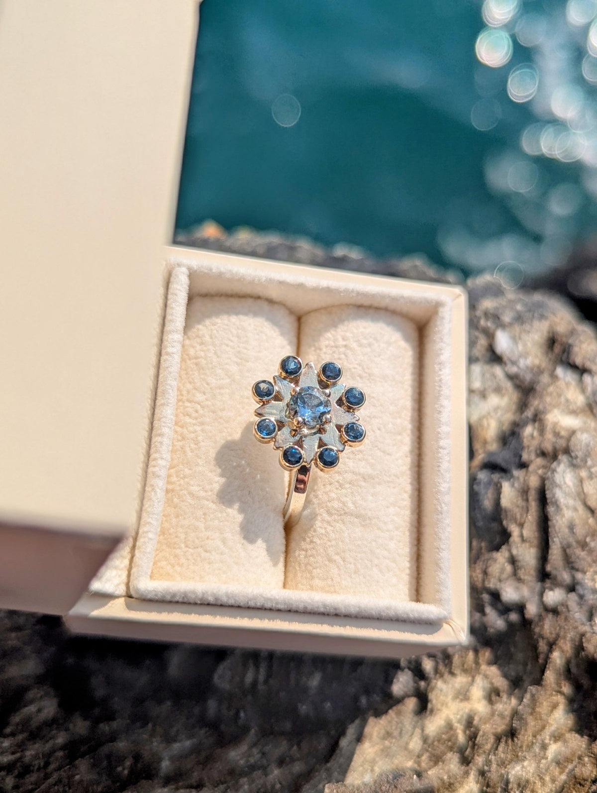 Blue topaz cluster ring displayed in a jewellery box beside the sea. 