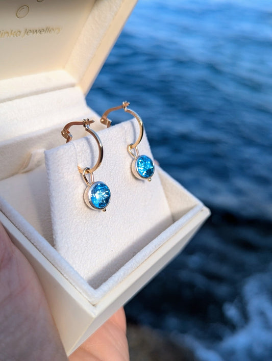 9ct gold hoop earrings with removable blue topaz charms in an open ivory jewellery box with ocean background handmade by Booblinka Jewellery