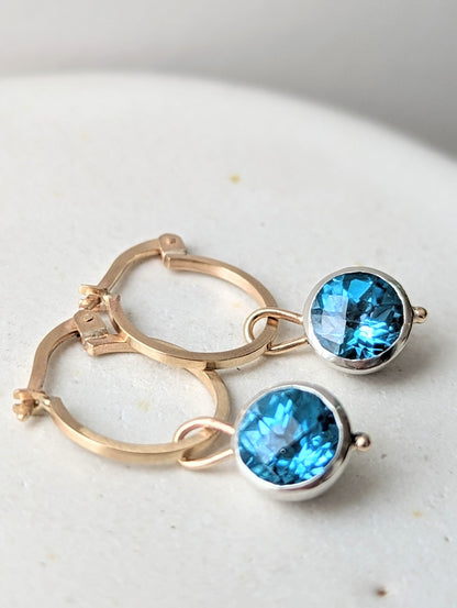 Detail of 9ct gold hoop earrings with removable blue topaz charms on an ivory jewellery box handmade by Booblinka Jewellery