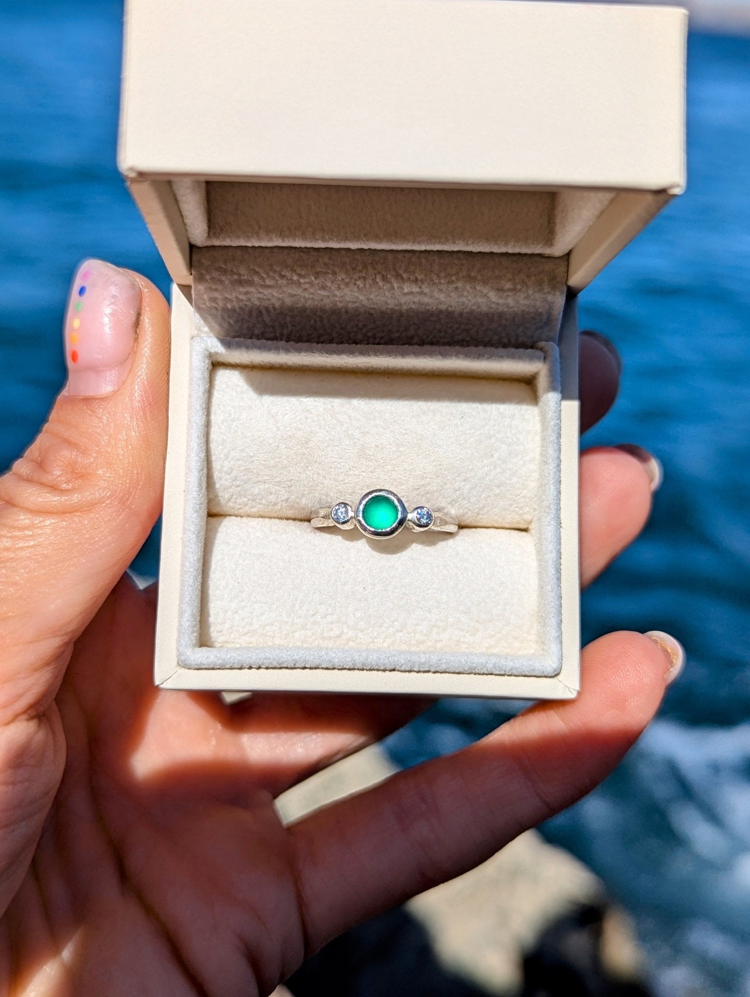 Green Sea Glass and Moissanite Engagement Silver Ring from Allure Collection in a plush ivory jewellery box above the ocean by Booblinka jewellery