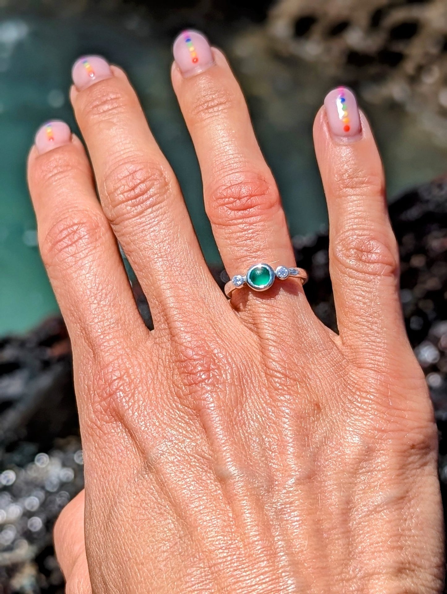 Green Sea Glass and Moissanite Engagement Silver Ring from Allure Collection on a hand above the ocean by Booblinka jewellery