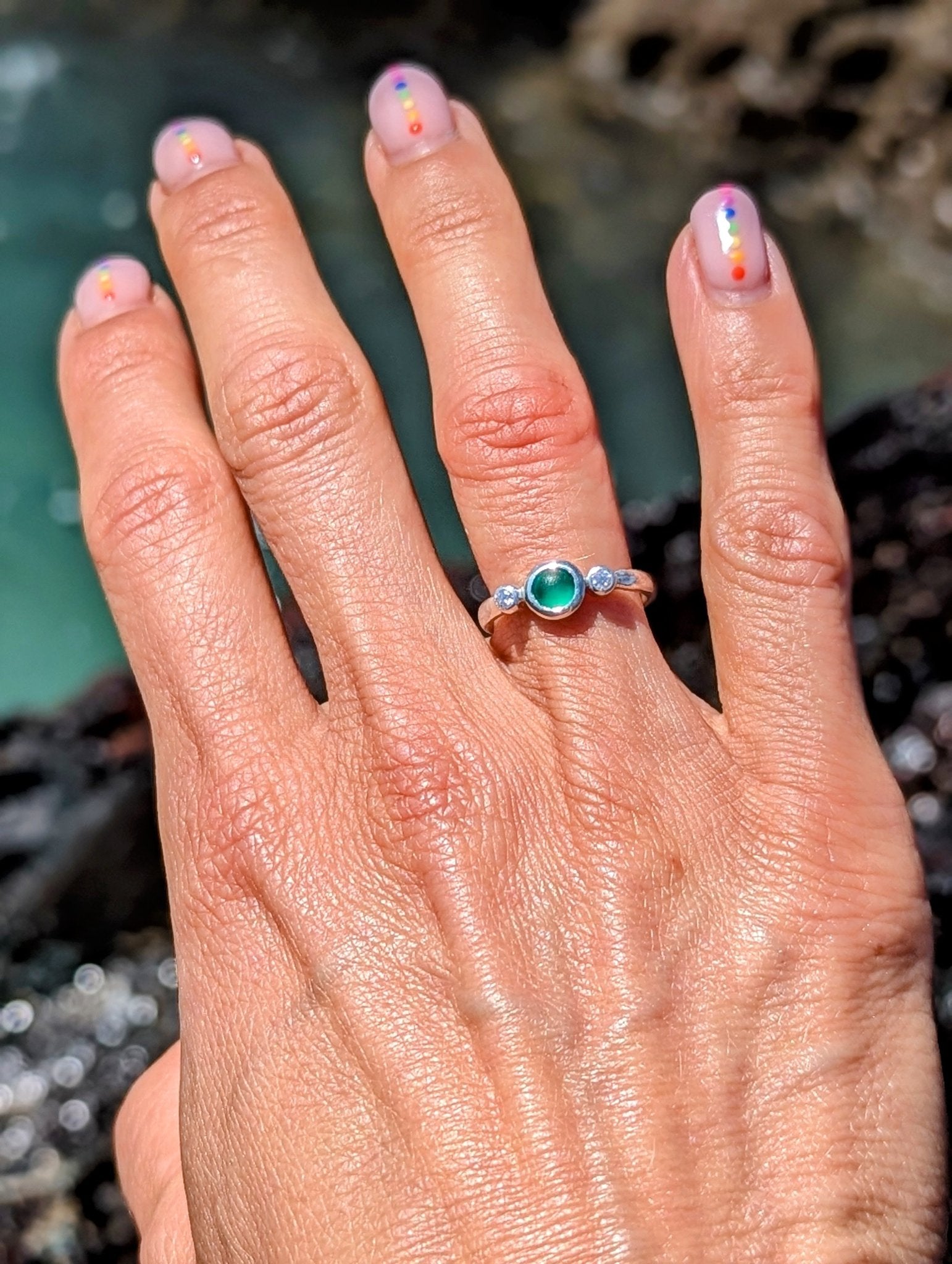Green Sea Glass and Moissanite Engagement Silver Ring from Allure Collection on a hand above the ocean by Booblinka jewellery