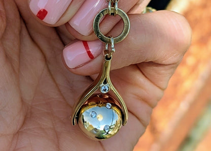 Gold necklace with a spinning pendant with diamonds held by a hand with pink nail polish.
