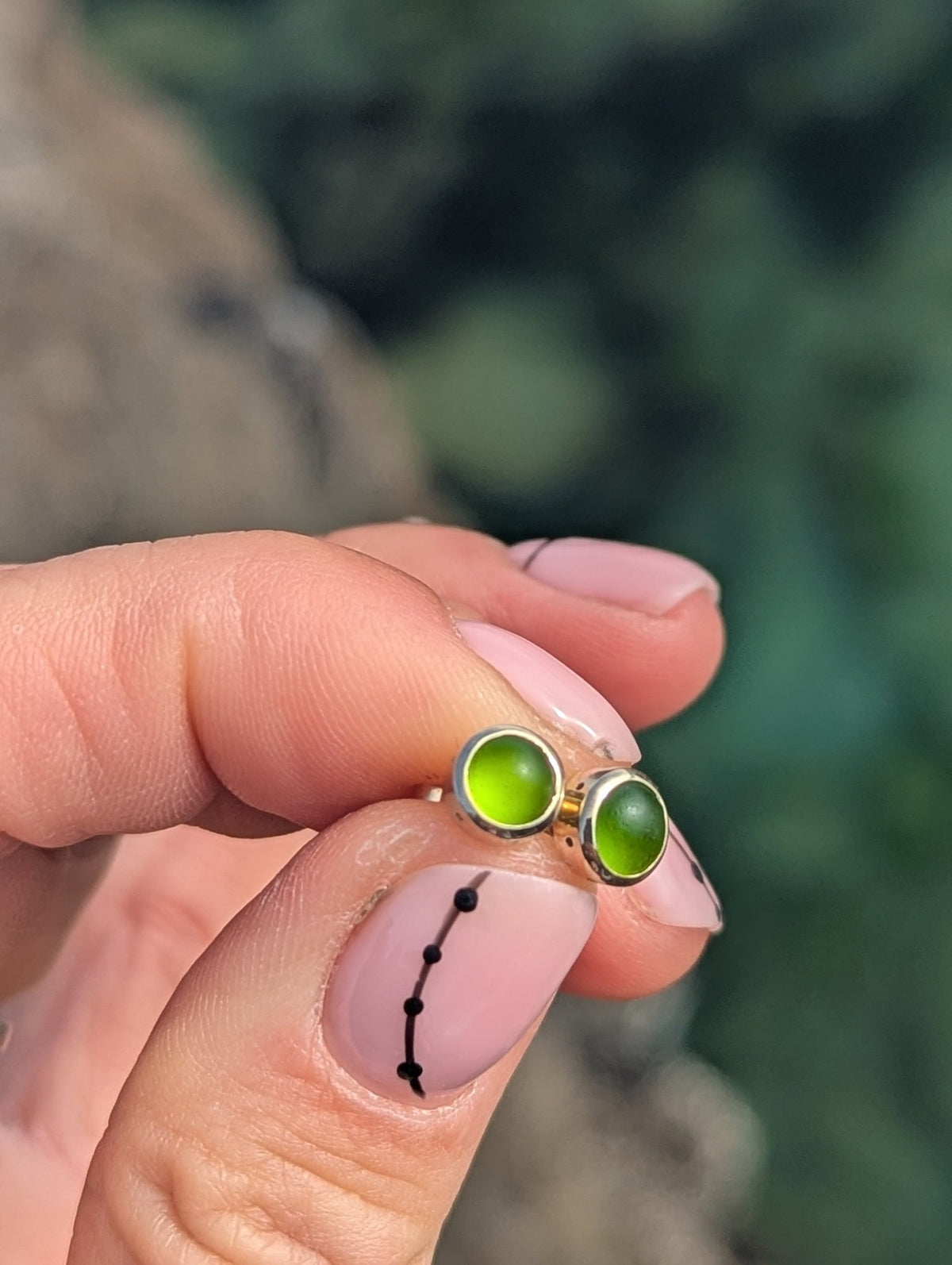 Close-up of a green sea glass stud earring held between the fingers, showing the gold setting and bright green colour.