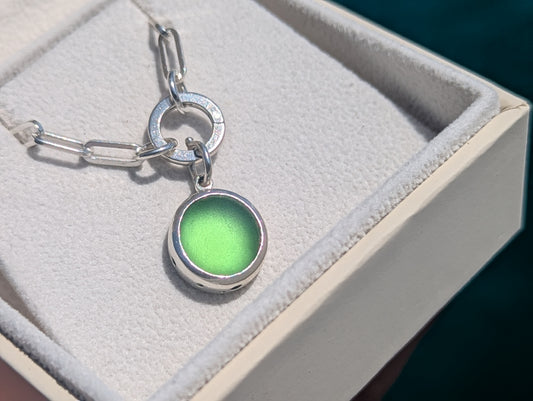 Genuine green sea glass pendant in sterling silver attached to a hinged charm holder on a sterling silver paperclip chain inside a cream jewellery box.