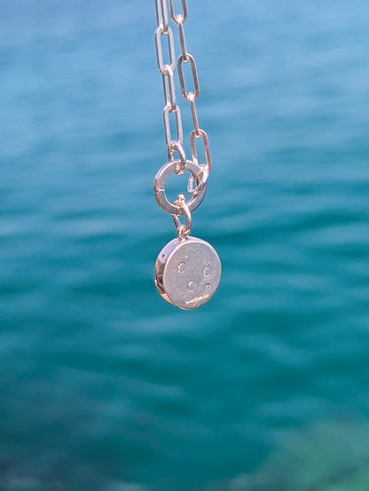 Back of a sterling silver green sea glass pendant showing the hand-stamped three bubbles and polished finish.