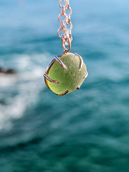 Green sea glass pendant on a silver chain with the sea behind