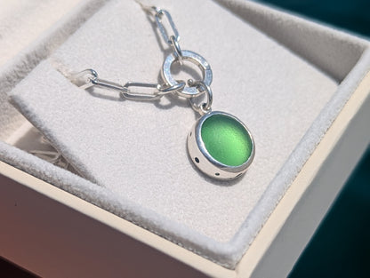 Side view of a genuine green sea glass pendant in sterling silver showing the depth of the handmade setting and bubble details around the edge.