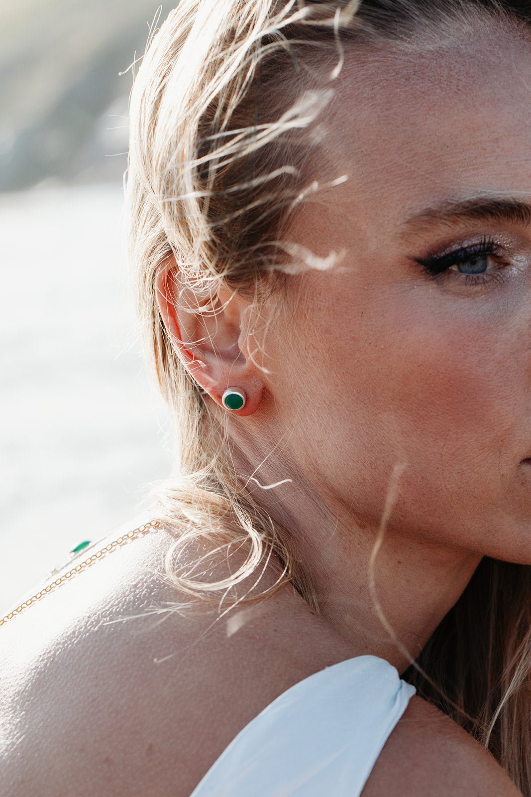 Blonde Woman wearing small round green sea glass stud earrings, showing their size on the ear.