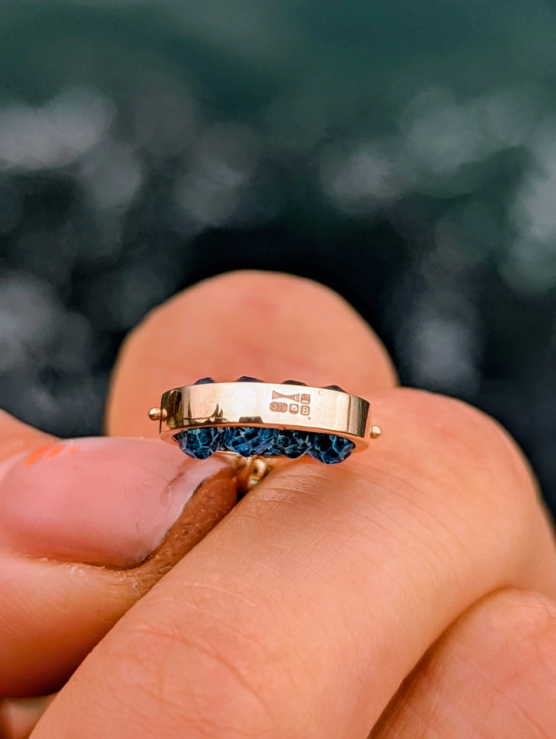 Side view of the 9ct gold HALO pendant showing its London hallmark and the four faceted blue topaz gemstones.