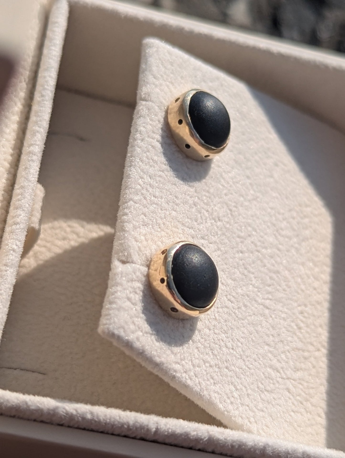 Close-up of the matching black sea glass stud earrings in solid yellow gold, showing the smooth opaque sea glass and handmade settings.