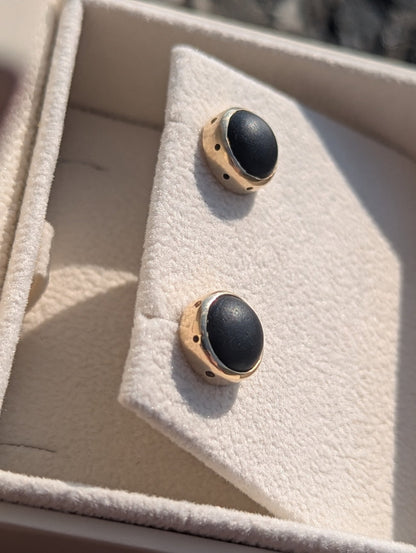 Close-up of the matching black sea glass stud earrings in solid yellow gold, showing the smooth opaque sea glass and handmade settings.