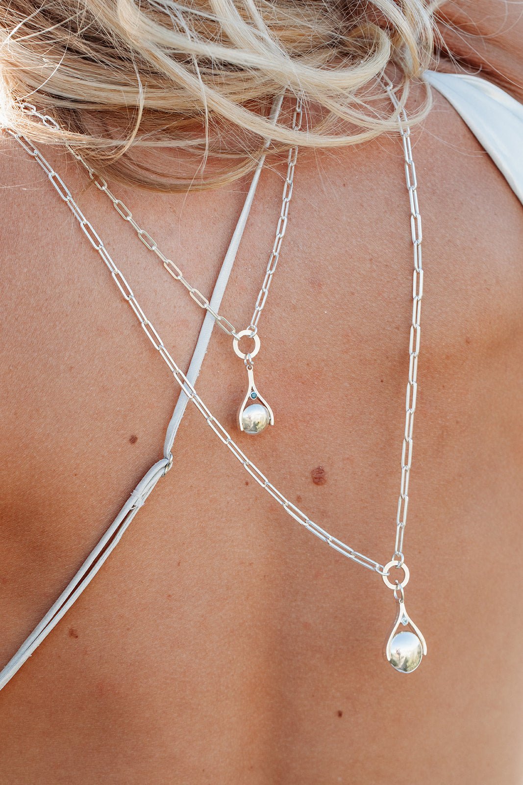 Woman wearing two silver spinning necklaces on her back with paperclip chains made by Booblinka Jewellery in Cornwall.