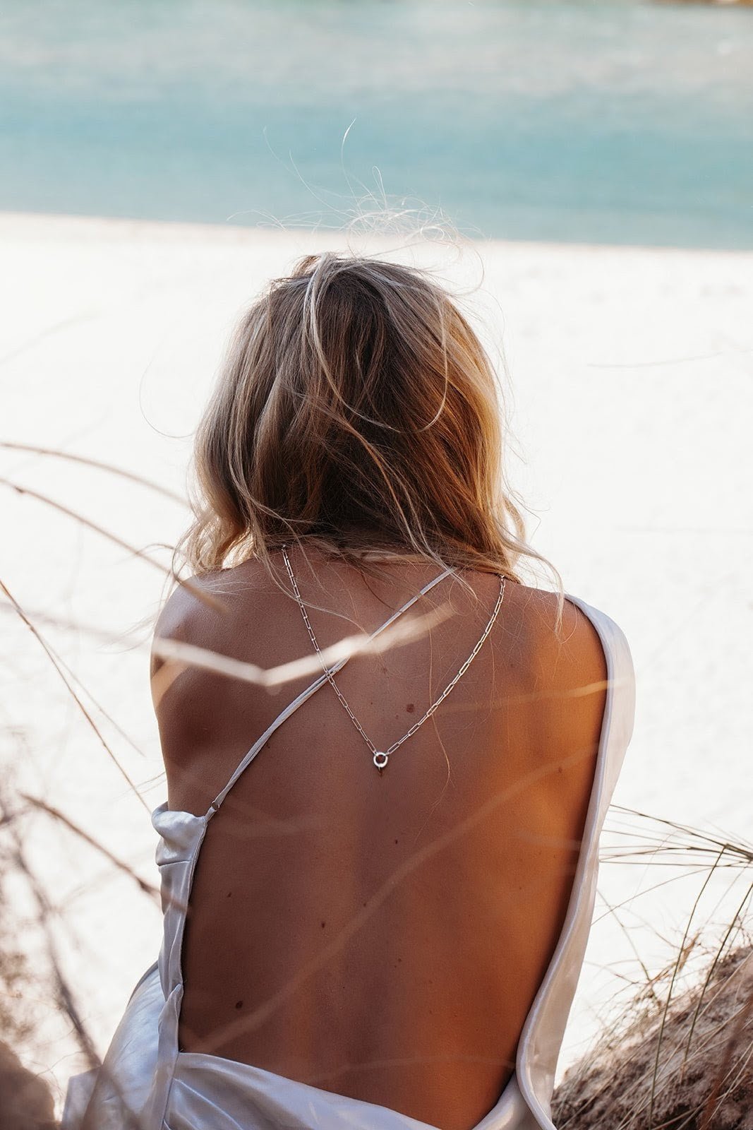 Woman sitting on the beach wearing on her back silver paperclip chain with connector made by Booblinka Jewellery in Cornwall
