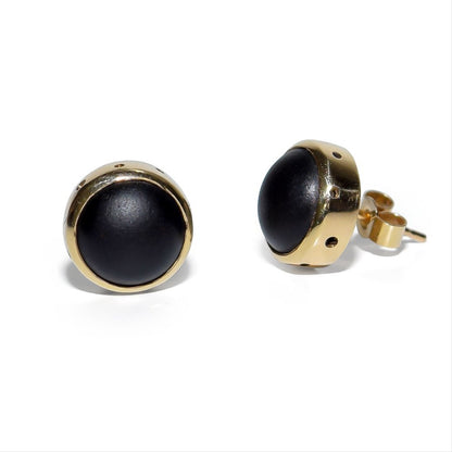 Close-up of two opaque black sea glass stud earrings in handmade 9ct yellow gold bezel settings with small gold bubble details.