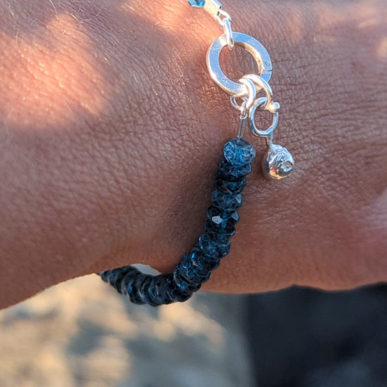 Close-up of a handmade sterling silver bracelet with faceted London Blue Topaz beads and a removable droplet charm.