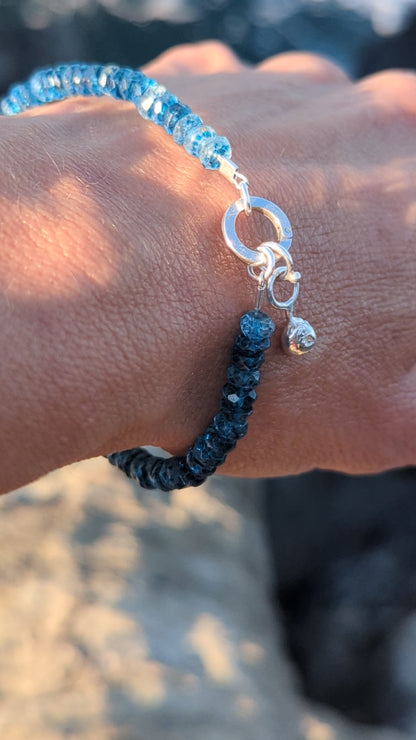 Close-up of a handmade sterling silver bracelet with faceted London Blue Topaz beads and a removable droplet charm.