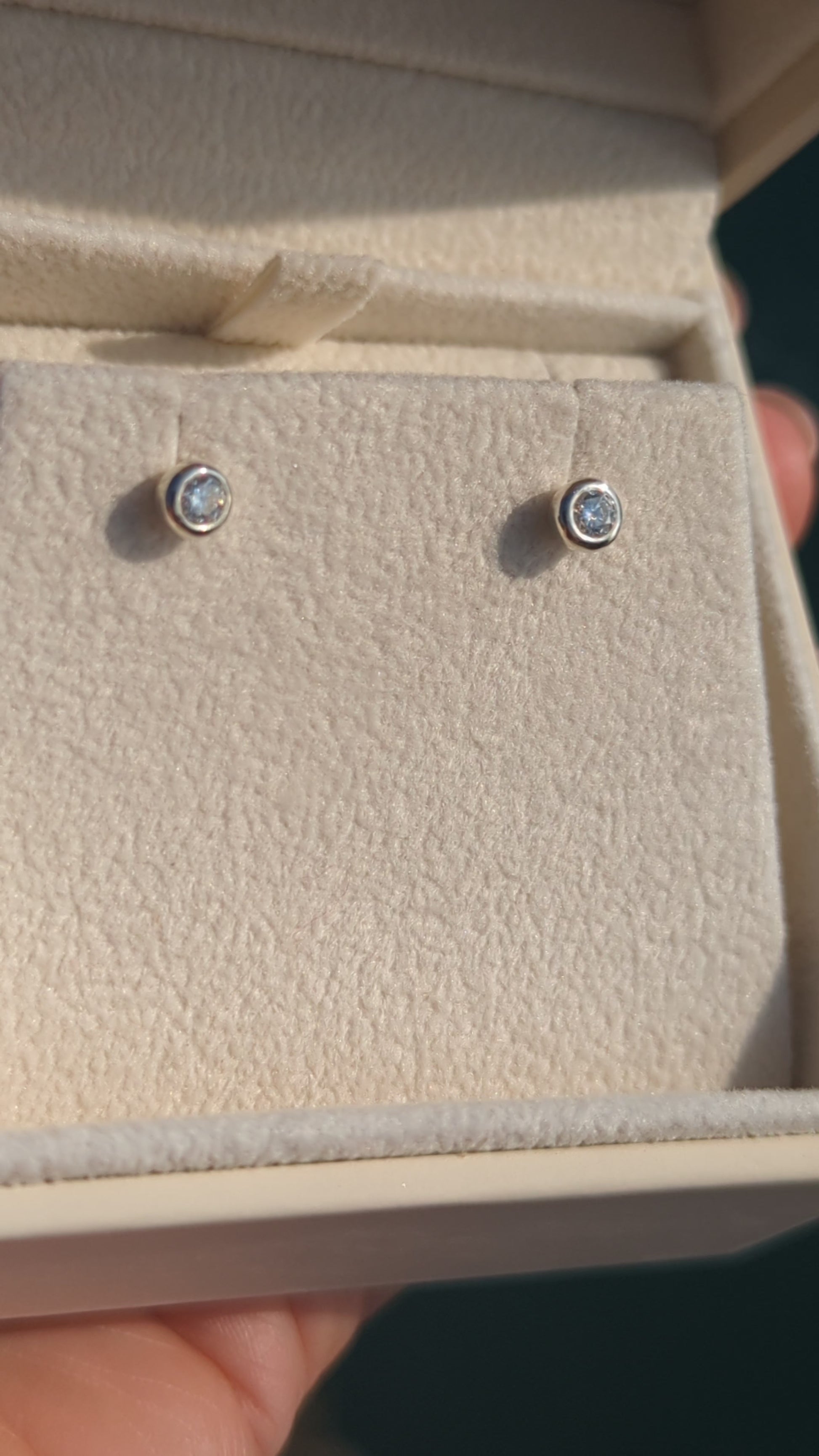 Silver stud moissanite earrings in a plush jewellery box above shimmering ocean in background made by Booblinka Jewellery
