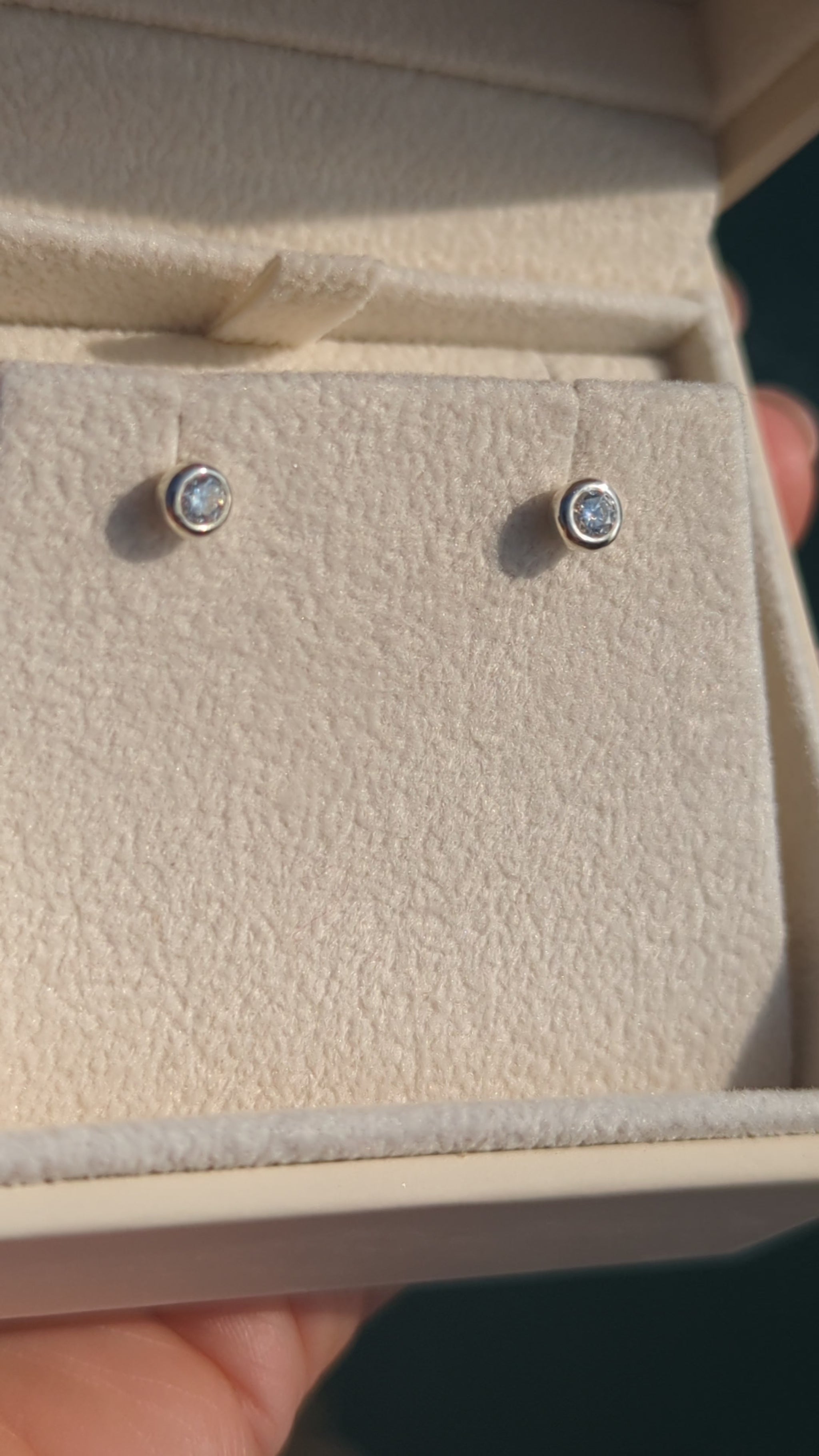Silver stud moissanite earrings in a plush jewellery box above shimmering ocean in background made by Booblinka Jewellery