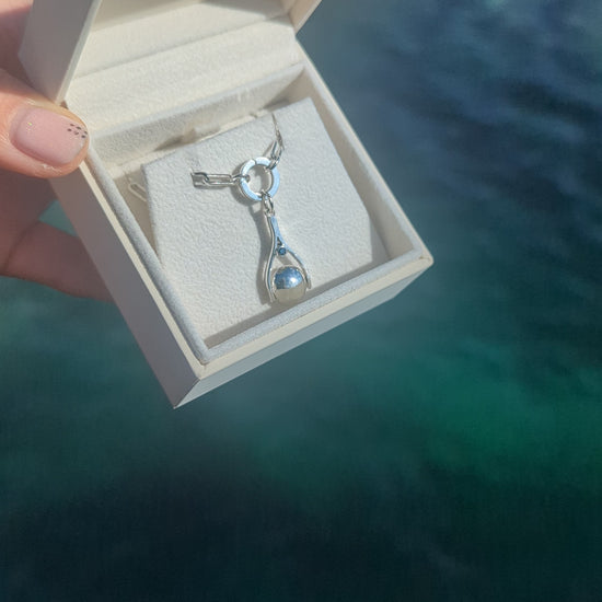 Silver mini spinning minstrel necklace with blue diamonds made by Booblinka Jewellery in a jewellery box above the ocean in Cornwall