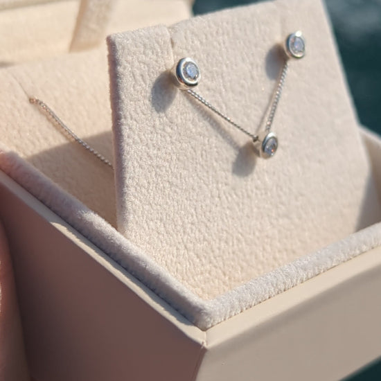 Silver stud moissanite earrings with the same necklace in a plush jewellery box above shimmering ocean in background made by Booblinka Jewellery