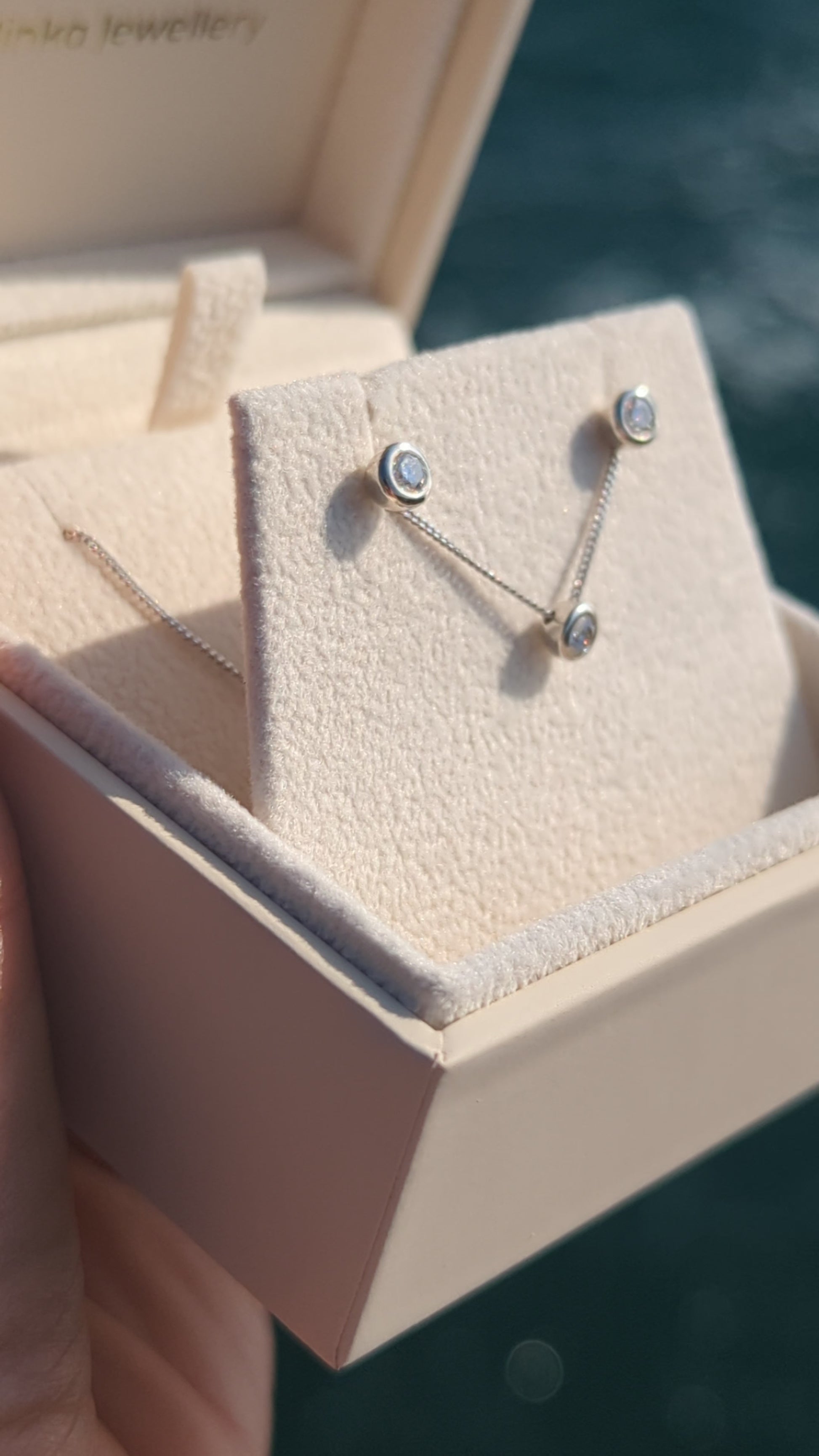 Silver stud moissanite earrings with the same necklace in a plush jewellery box above shimmering ocean in background made by Booblinka Jewellery