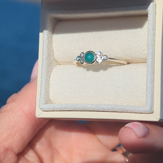 video of White gold ring with a teal sea glass and six diamonds in a jewellery box held by a hand against a blue ocean made by Booblinka Jewellery