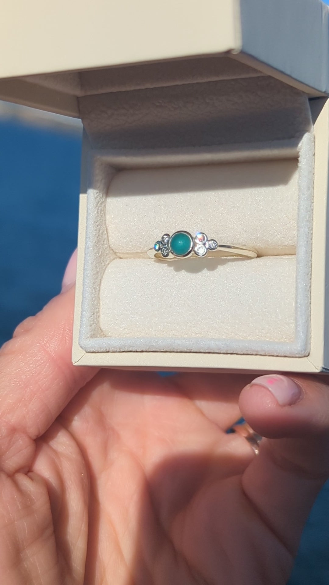 video of White gold ring with a teal sea glass and six diamonds in a jewellery box held by a hand against a blue ocean made by Booblinka Jewellery