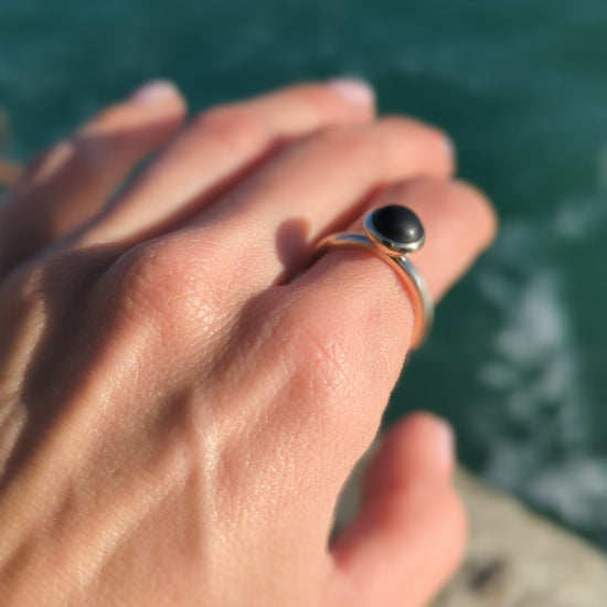 Pirate Black Sea Glass Gold Ring on a hand above the ocean