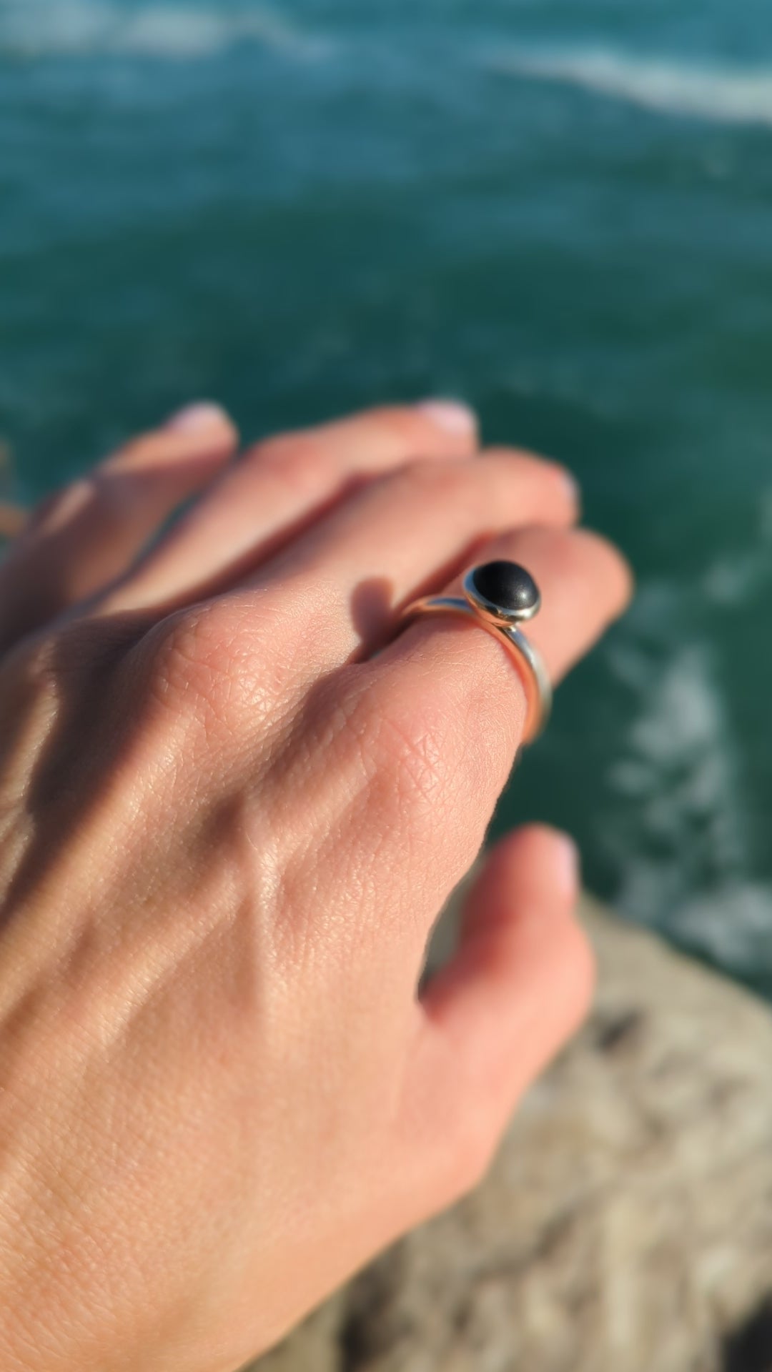Pirate Black Sea Glass Gold Ring on a hand above the ocean
