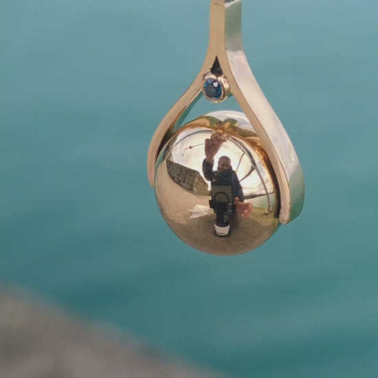 Close-up video of a handmade spinning gold necklace with blue diamonds, rotating pendant design inspired by the ocean made by Booblinka Jewellery