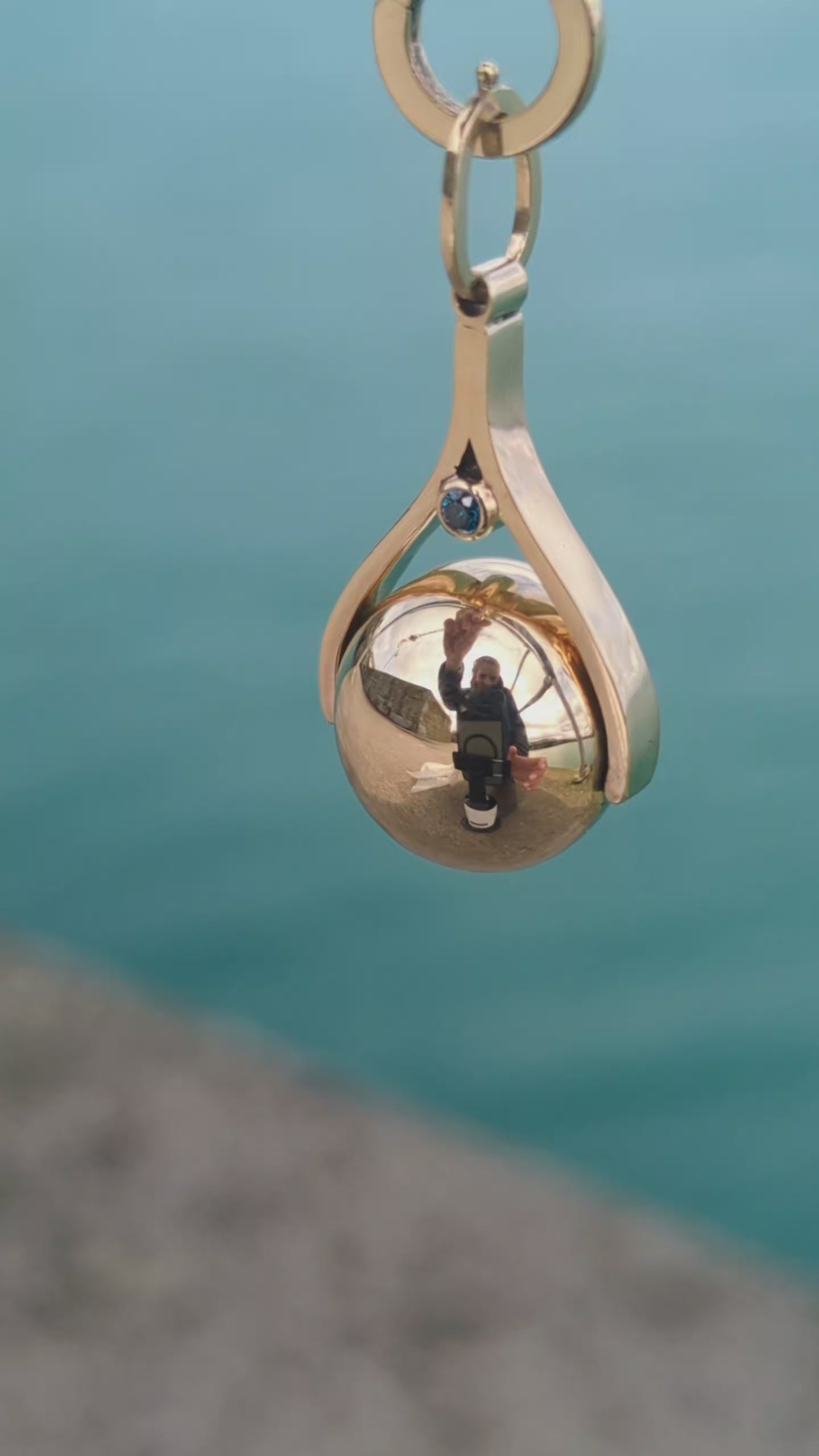 Load video: Close-up video of a handmade spinning gold necklace with blue diamonds, rotating pendant design inspired by the ocean made by Booblinka Jewellery