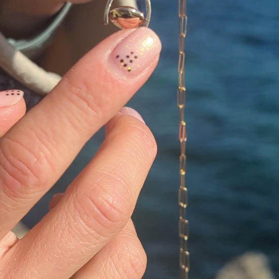 mini spinning minstrel necklace made by Booblinka Jewellery spinning above the ocean in Cornwall